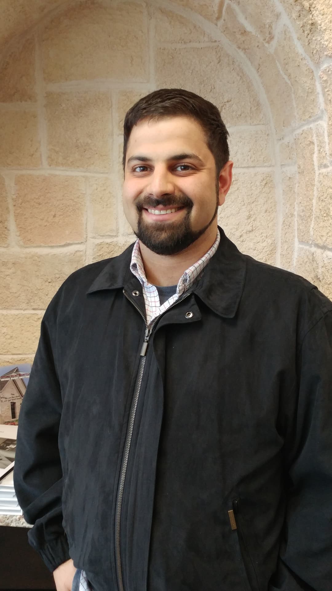 A bust shot of Alex standing in front of a nice wall.
